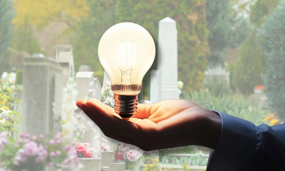 Illustration of a hand holding a light bulb against the background of a cemetery