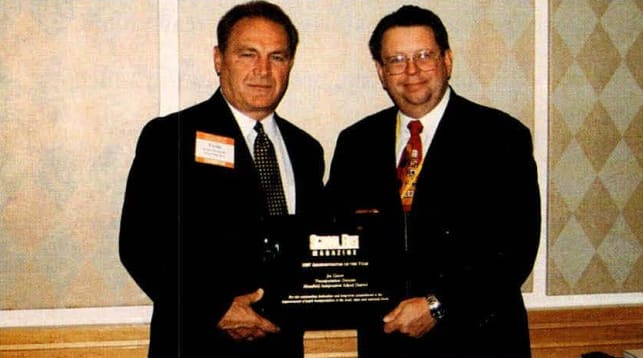 two men in black suits stand together for an award presentation