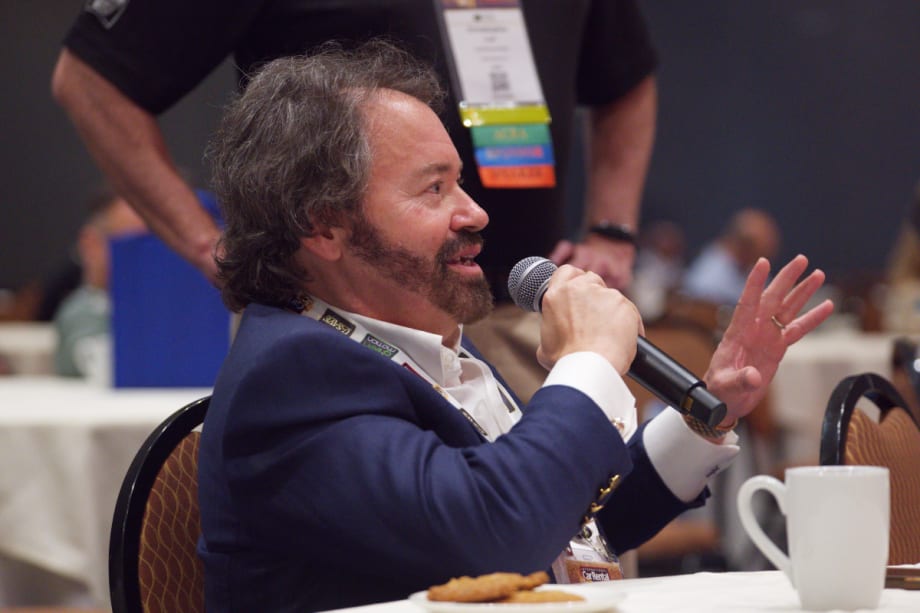 John Possumato holding microphone while asking a question during a live conference session at the ICRS Show.