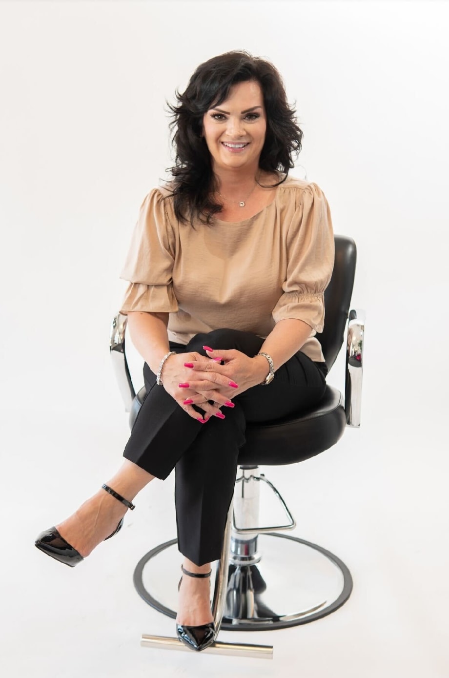 A woman with black hair sits in a salon chair, with crossed legs.