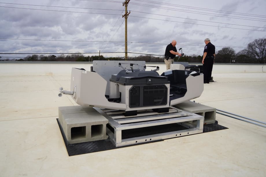 Two police officers stand near a rooftop drone launch system, preparing equipment for a first responder program providing aerial support to emergency calls.