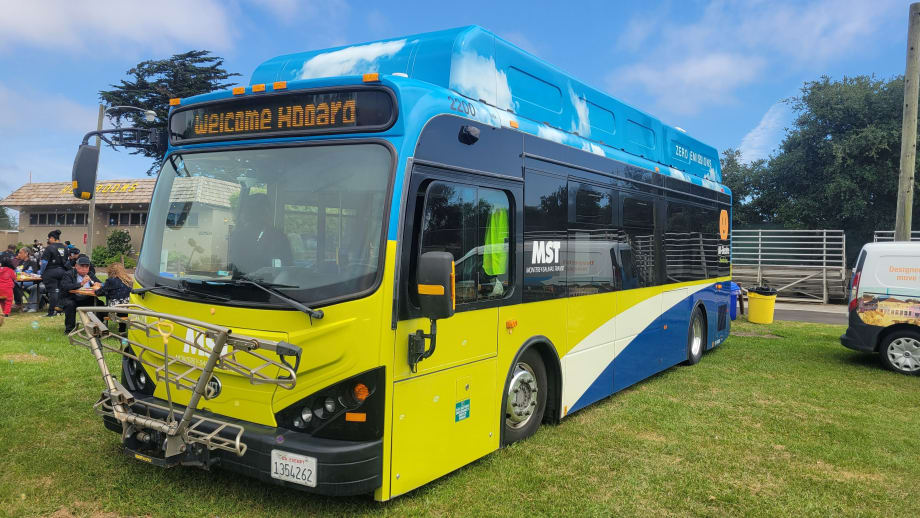 A light green and blue MST public transit bus parked on grass.