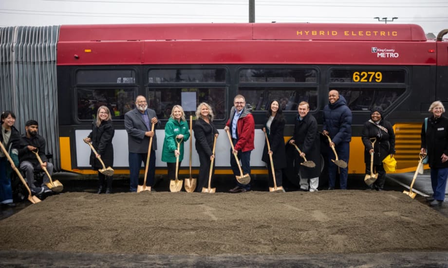 County and agency officials break ground in front of a red and yellow King County Metro public transit bus.