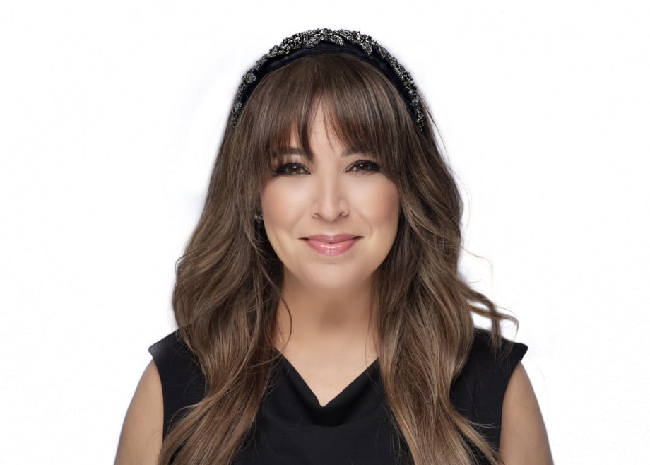 A woman with long brown hair, a black sleeveless blouse, and a beaded headband.