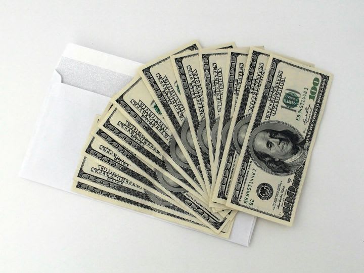 A fan of $100 bills sitting on a white envelope