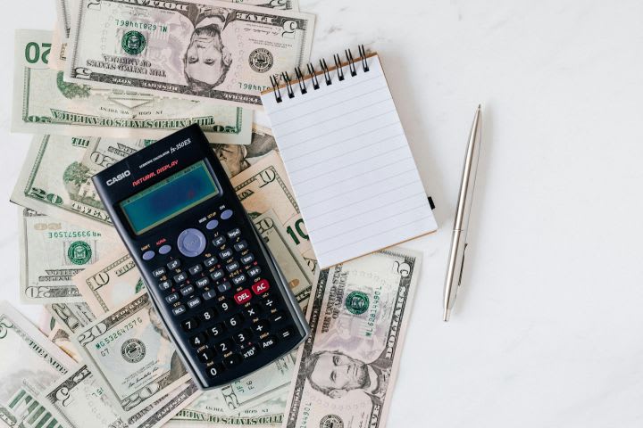 Photo of paper money bills, a calculator, notepad and pen