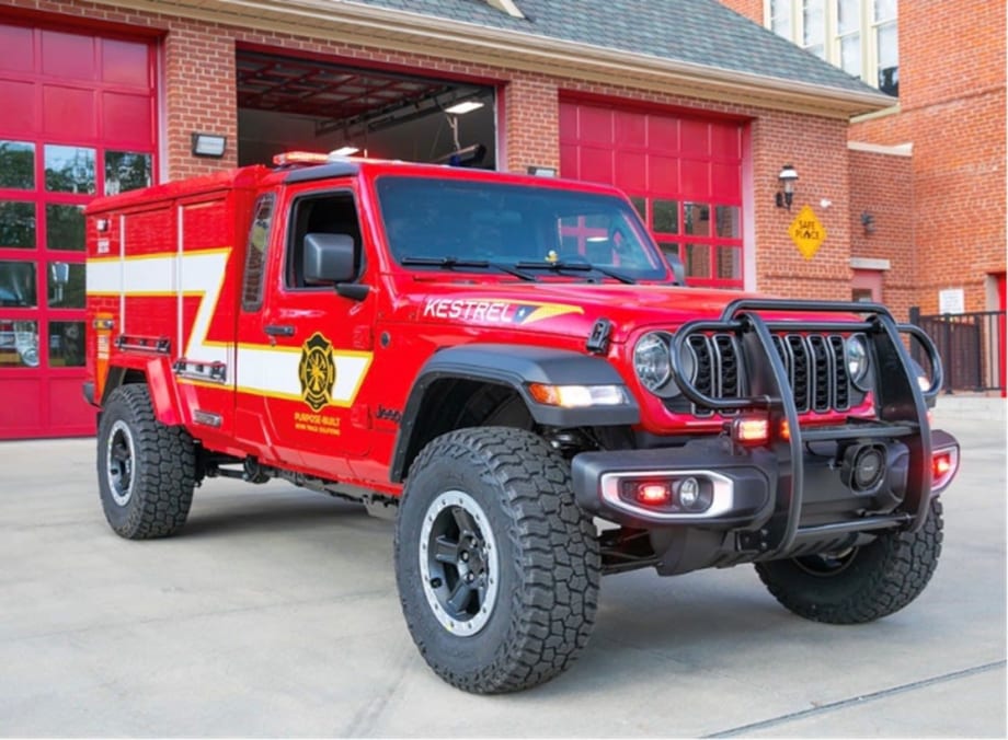 Red Morgan Olson Kestrel fire response truck parked outside a fire station, featuring off-road tires, emergency lights, and equipment compartments for first responder use.