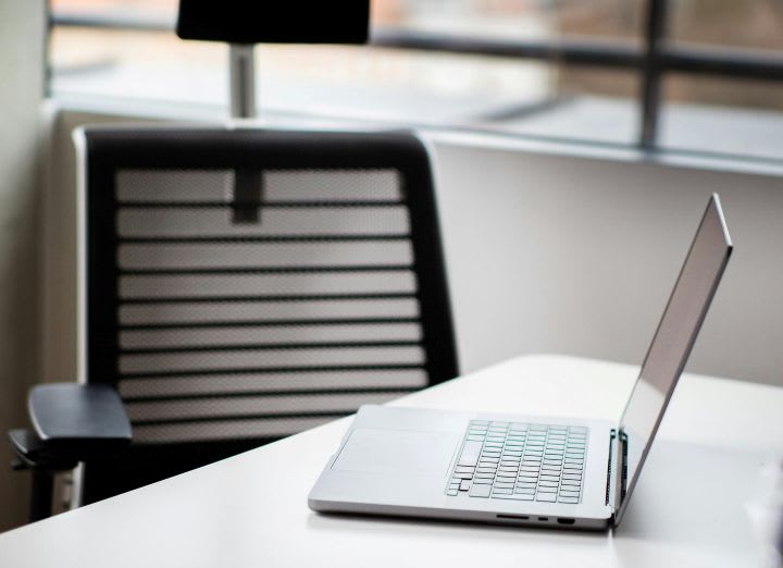 Laptop computer open on desk with empty chair behind it