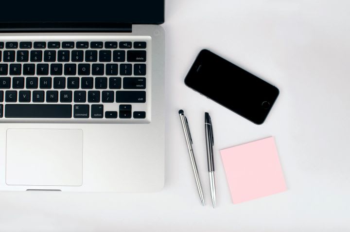 Photo of laptop on desk with pens, phone and sticky notepad beside it