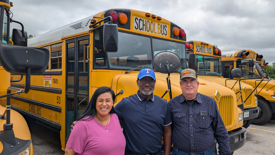 Three people pose in front of a line of school buses.