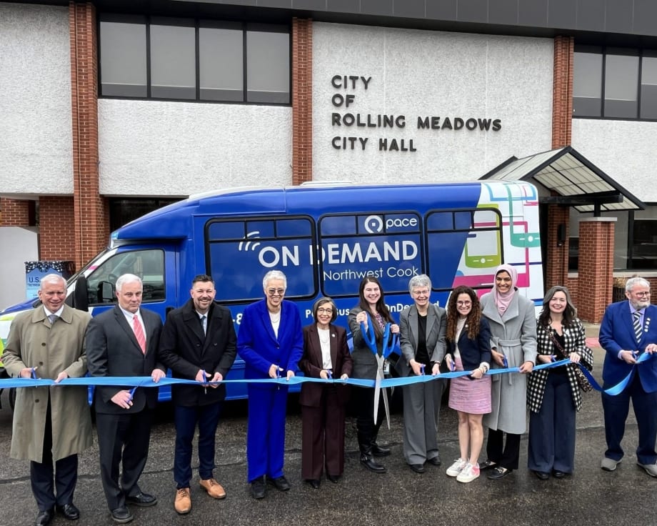 Officials and community leaders cut a ribbon in front of a Pace On Demand shuttle bus outside Rolling Meadows City Hall to celebrate expanded on-demand transit service in northwest Cook County.