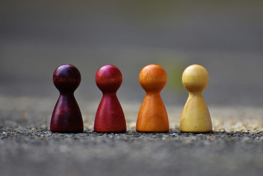 Wooden people figures of different colors in a row, similar to board game pieces