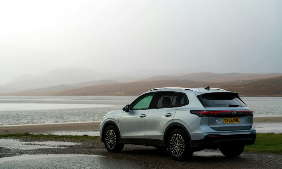 white SUV parked in front of a body of water with a gray sky background
