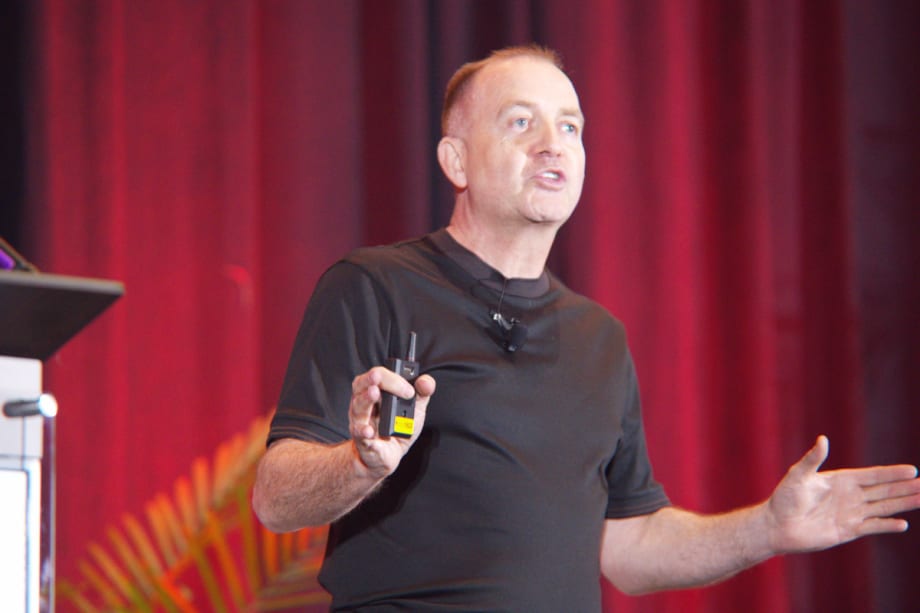 Richard Lowden gesturing on stage in front of a red curtain at the Gaylord Texan Resort near Dallas.