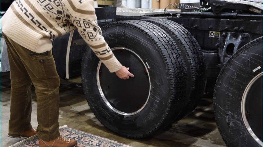 Dual truck tires with black aerodynamic wheel cover and a man bending down getting ready to take one off