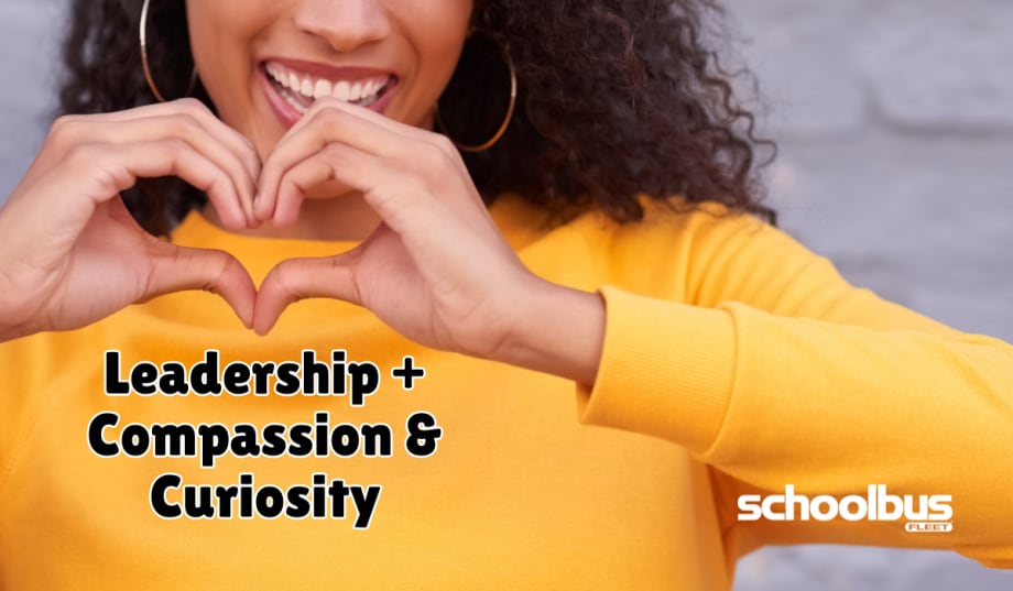 A smiling person in a yellow sweater forms a heart shape with their hands above the words "Leadership + Compassion & Curiosity." The graphic accompanies a School Bus Fleet feature on how empathy, compassion, and curiosity can strengthen leadership in student transportation.