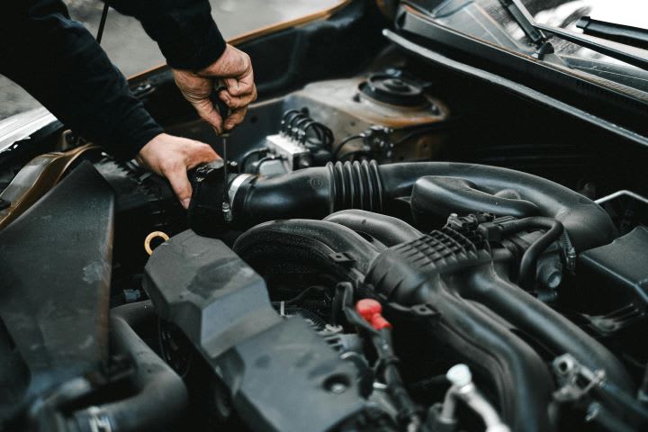 Photo of man working under the hood of a car with a tool