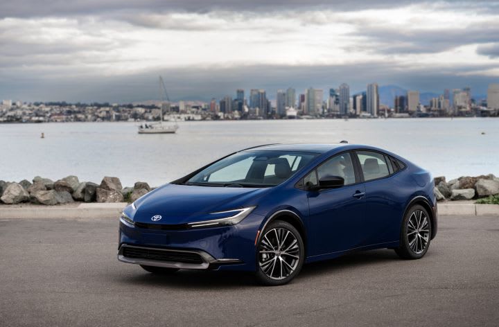 Photo of blue Toyota Prius parked next to body of water with city skyline in background