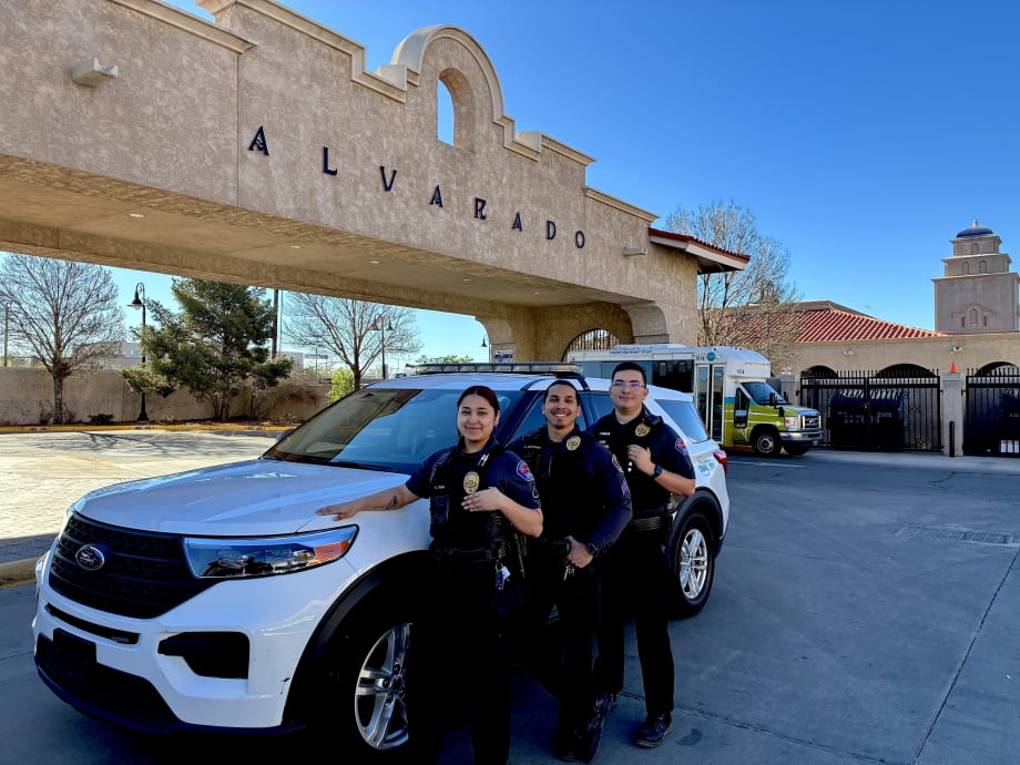 Three officers pose in front of a cruiser and sign that says Alvarado.
