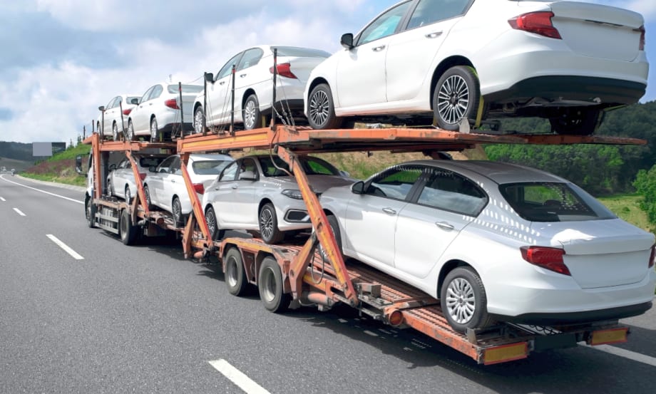 A double-decker stinger car hauler carries a full load of new white vehicles along an interstate highway.