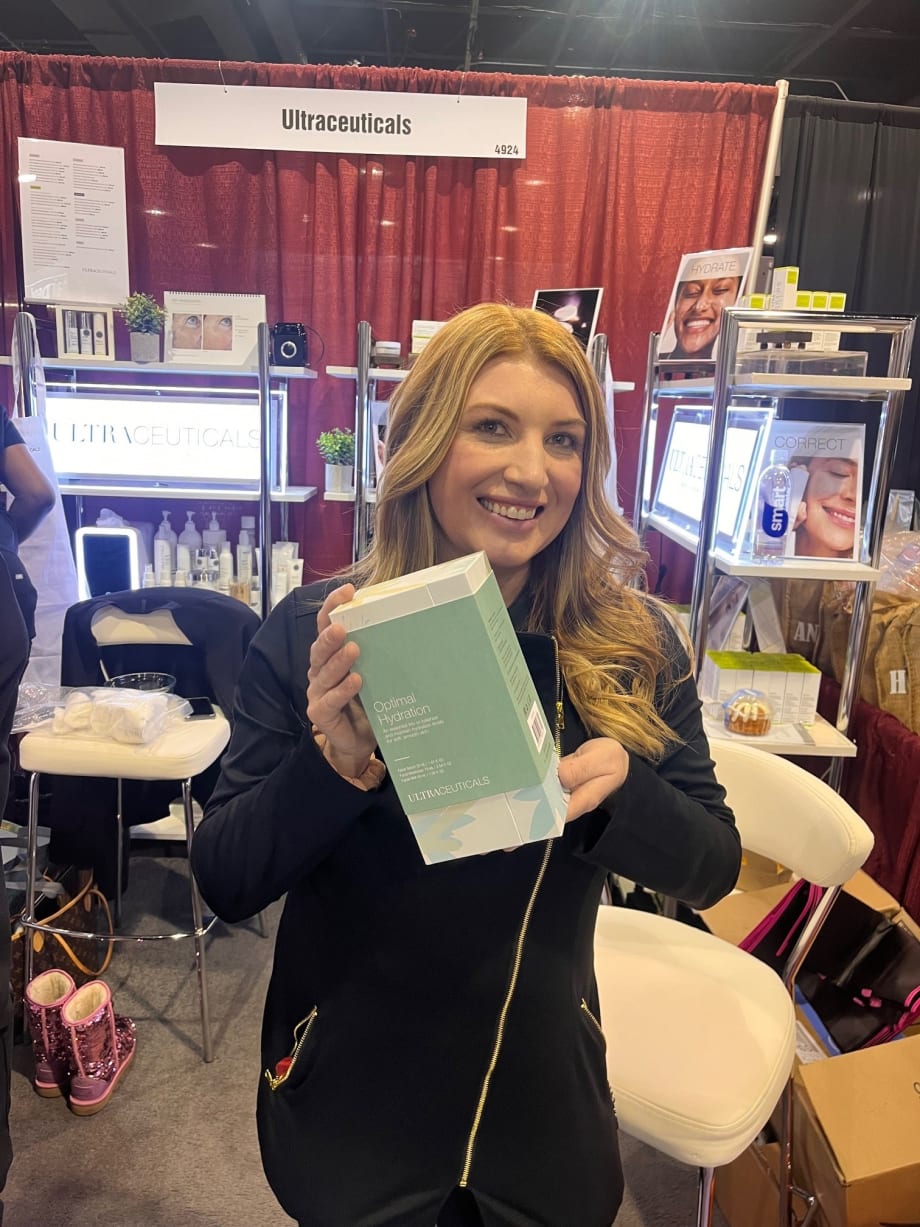 A woman smiles and holds a box of skincare products.
