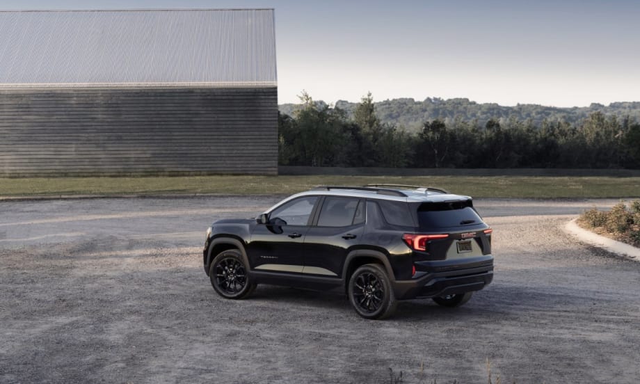 The back left side of a black 2025 GMC Terrain Elevation in front of a metal warehouse.