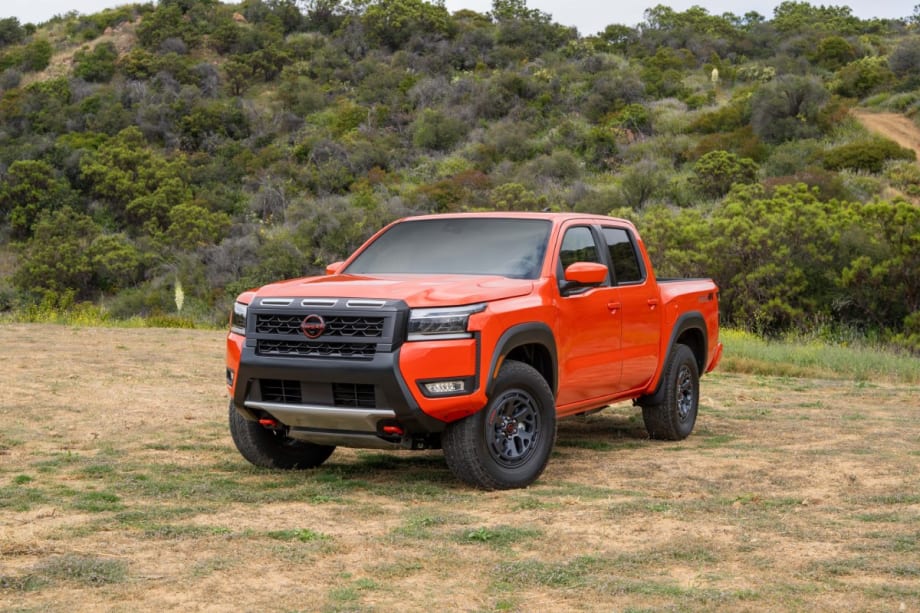 An orange Nissan Frontier in front of a hillside.