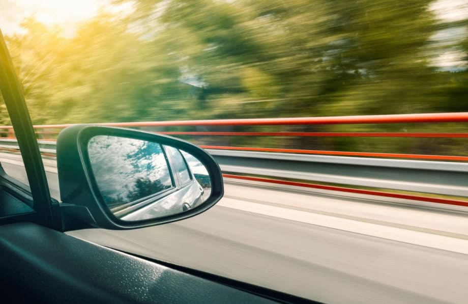 Image of a bridge and trees rushing by from inside of a moving car.