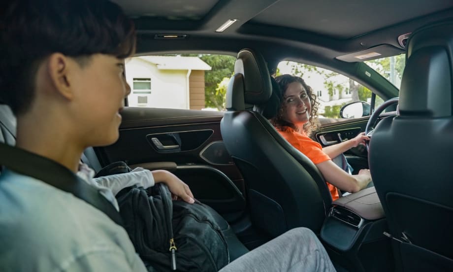Female HopSkipDrive CareDriver in an orange shirt driving a student to school in a car.