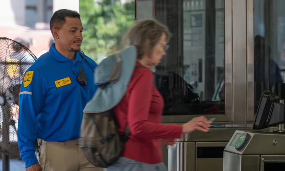 An MBTA fare engagement representative looks on while a woman pays for her subway fare.
