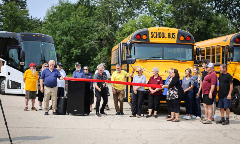A crowd stands behind a red ribbon being cut.