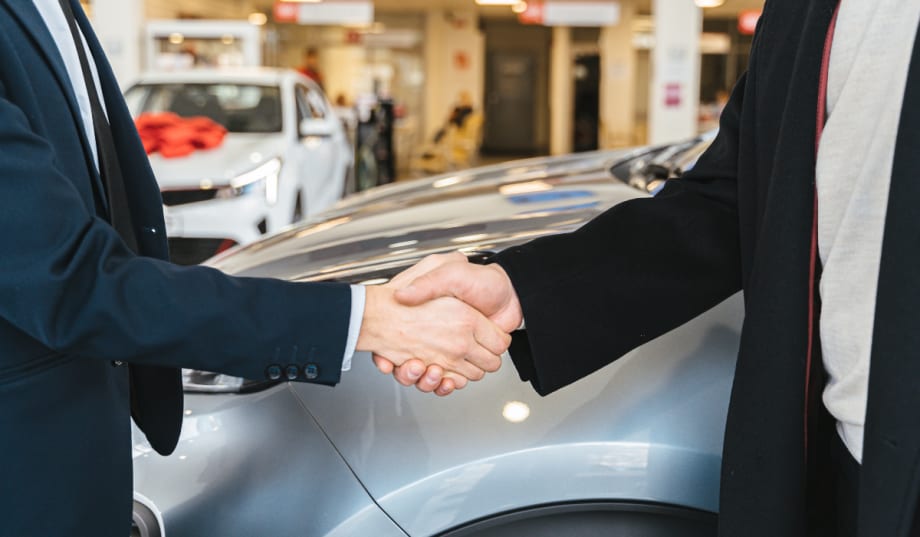 two men shaking hands in front of cars