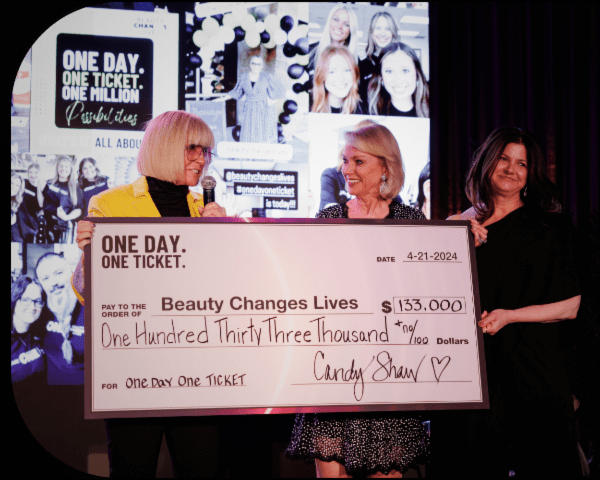 Two happy women, one wearing yellow blazer, are smiling and holding an oversized check.