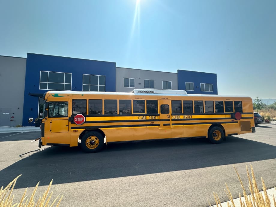 A yellow Blue Bird electric school bus sits in front of a school building.