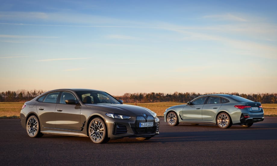 Two BMW i14s are posed on the open road in front of a sunset, with one facing away with a view of the back.