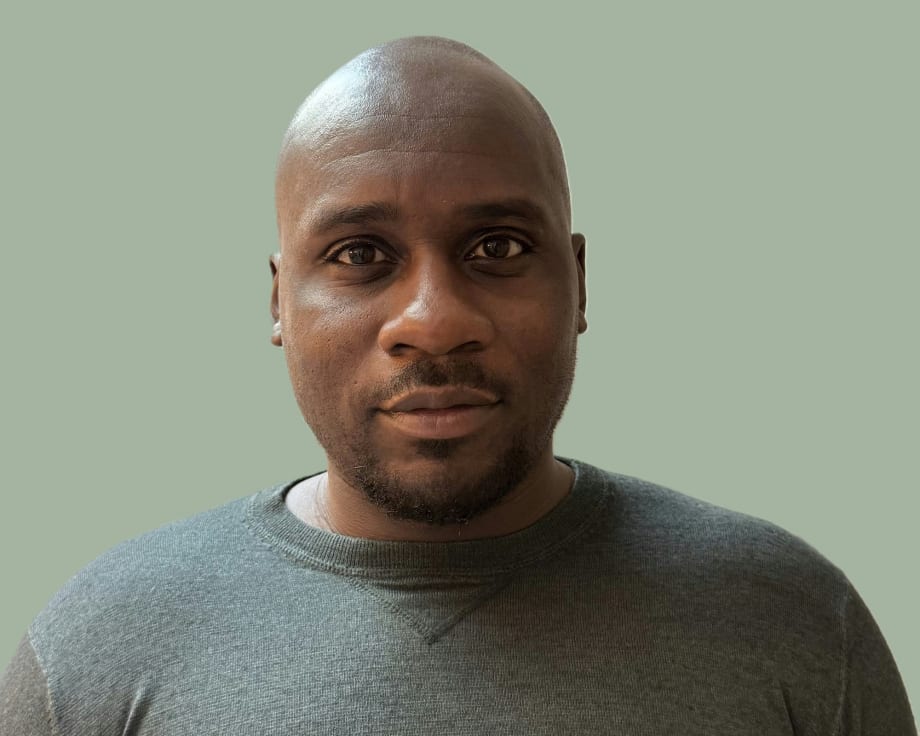 Bald man in gray sweater against sage green background