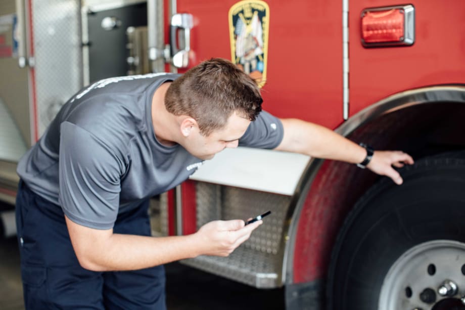 A firefighter with a phone looking at a fire truck wheel.