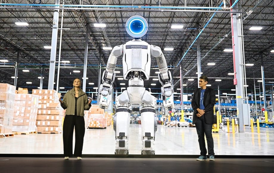 Boston Dynamics executives in front of image of Atlas humanoid robot in a warehouse setting