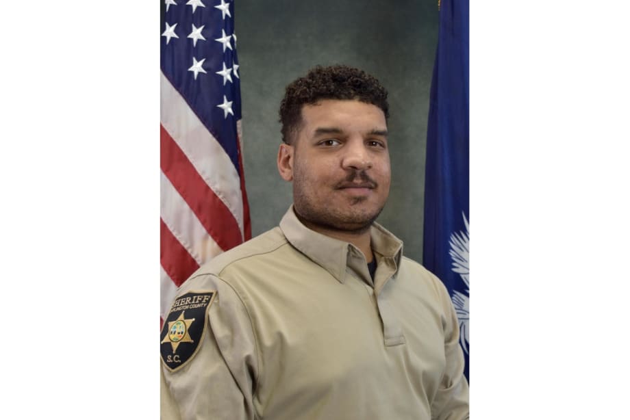 Sheriff's deputy in tan uniform posing with American and state flags