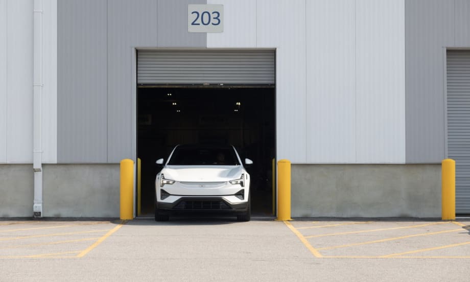 An image of the front end of a white Polestar 3 parking within the open frame of a commercial garage door.