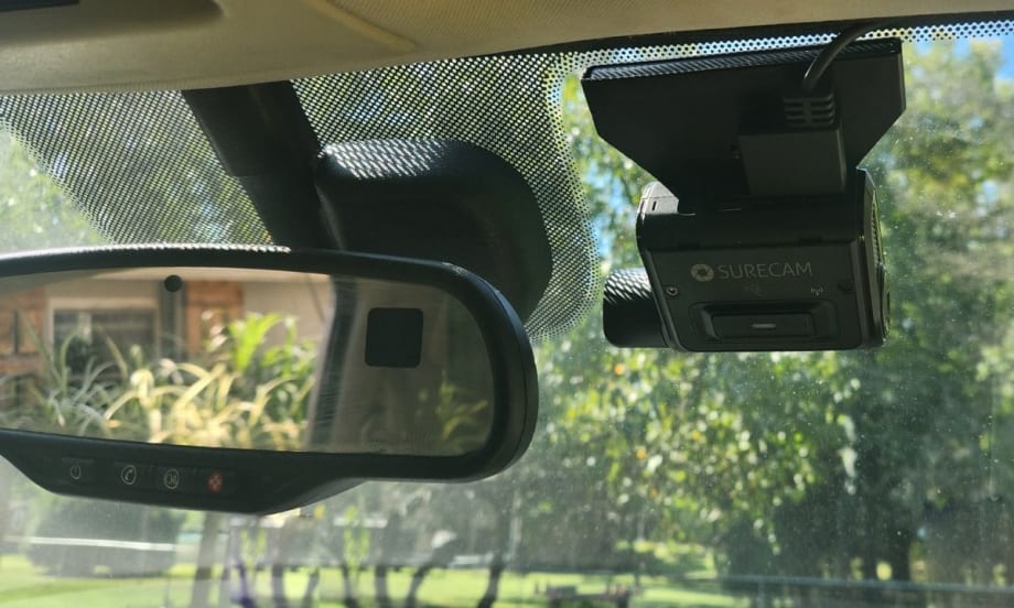 An image of the rearview mirror and a SureCam dashcam attached to the inside of a car windshield.