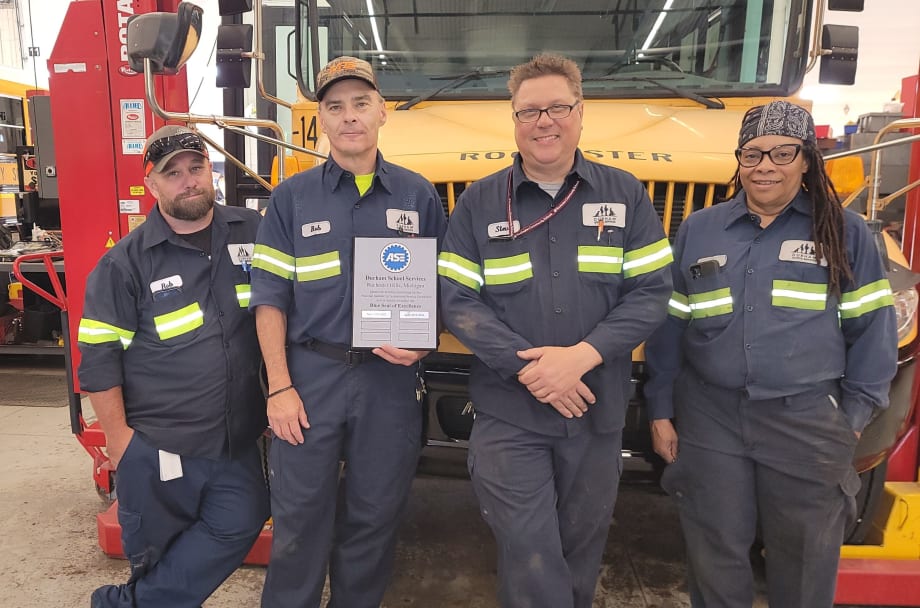Durham School Services Ann Arbor team with ASE Blue Seal of Excellence plaque in front of a school bus