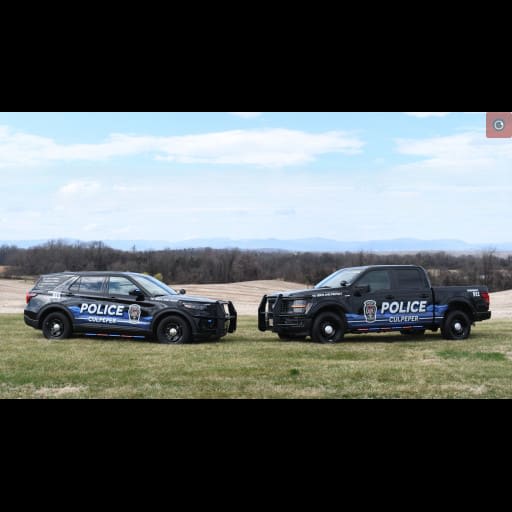 Two Culpeper Police vehicles, an SUV and pickup, display a new Blue Ridge Mountain-inspired design while parked on grass with a scenic landscape in the background.