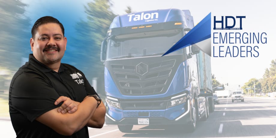 Hispanic man stands with arms crossed with electric Nikola truck in the background