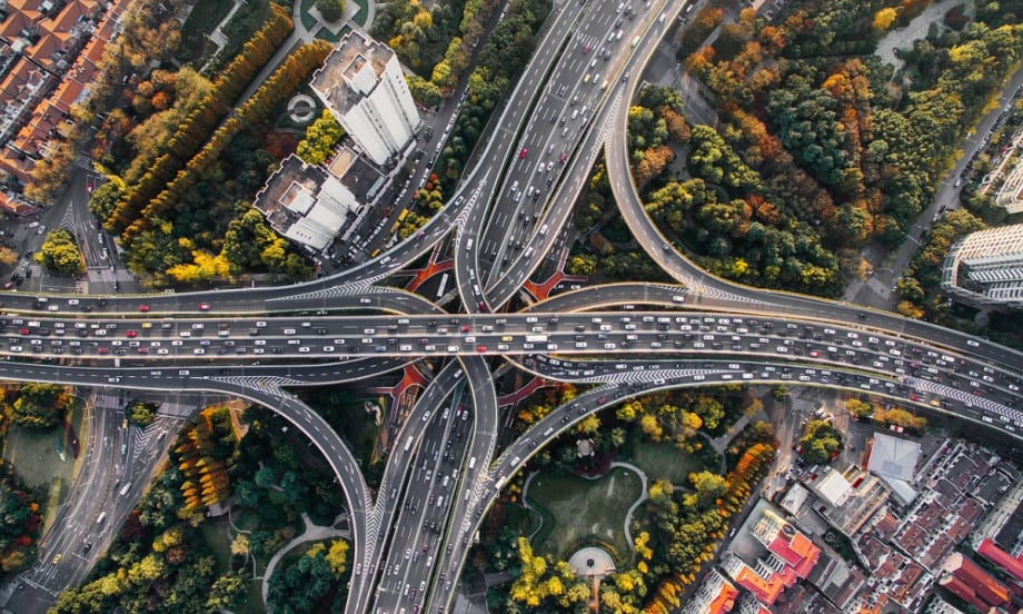 Aerial view of interconnected highways and exit ramps surrounded by trees, streets, and buildings.
