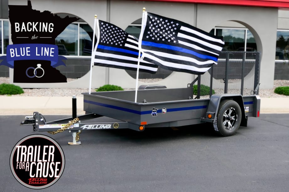 A dark gray dropdeck utility trailer with a thin blue line is shown, with 2 Thin Blue Line flags hanging off the back.