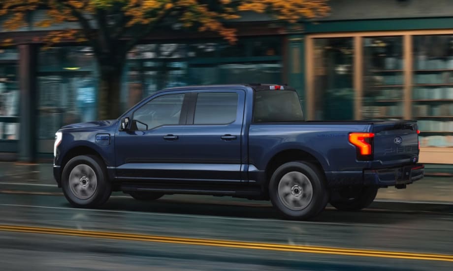 Blue Ford F-150 Lightning driving down the road in front of shops