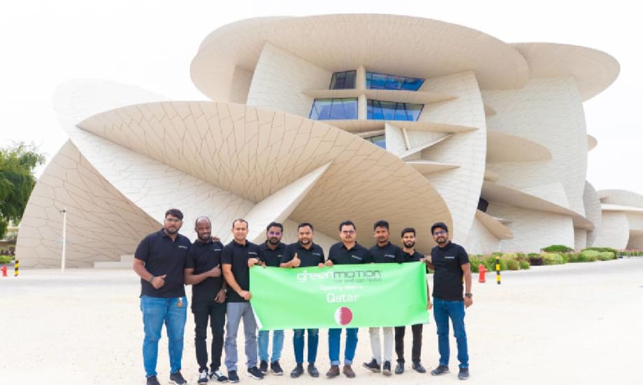 Green Motion team in front of Doah landmark with green banner.