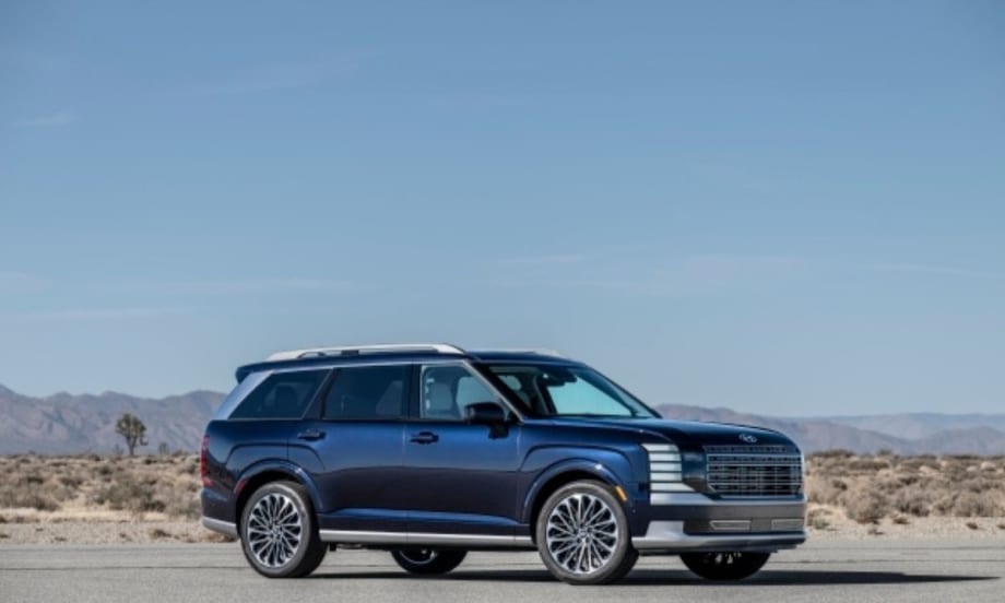 A dark blue full-size SUV parked on a desert road, with sleek modern styling, large alloy wheels, and a chrome-accented grille, set against a backdrop of dry desert landscape.