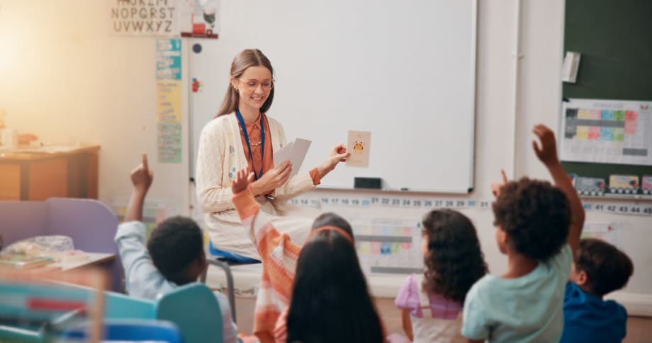 A female teacher sitting in front of elementary school classroom, giving a lesson to several students.